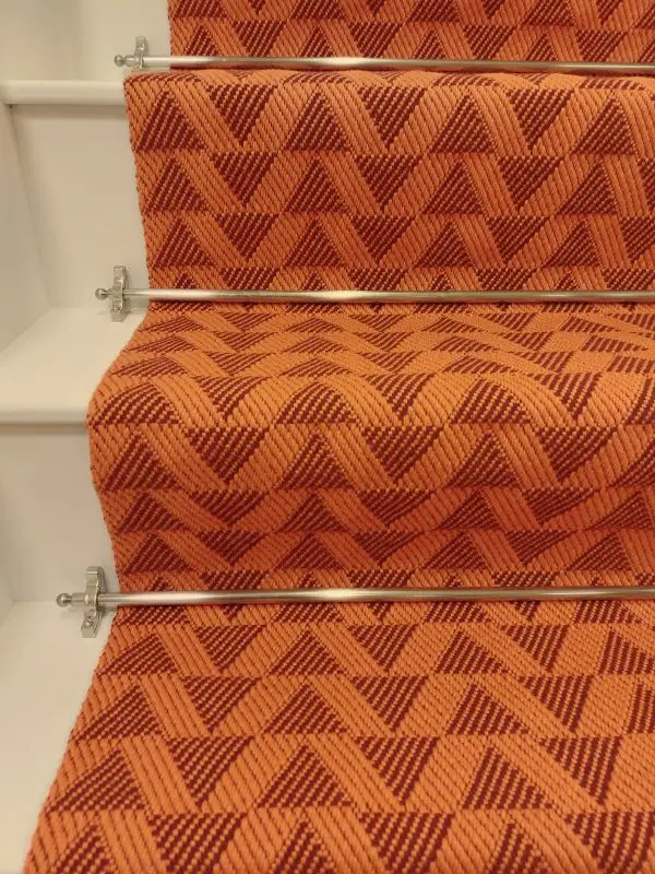 Bright orange stair runner with red triangle pattern on white wooden stairs