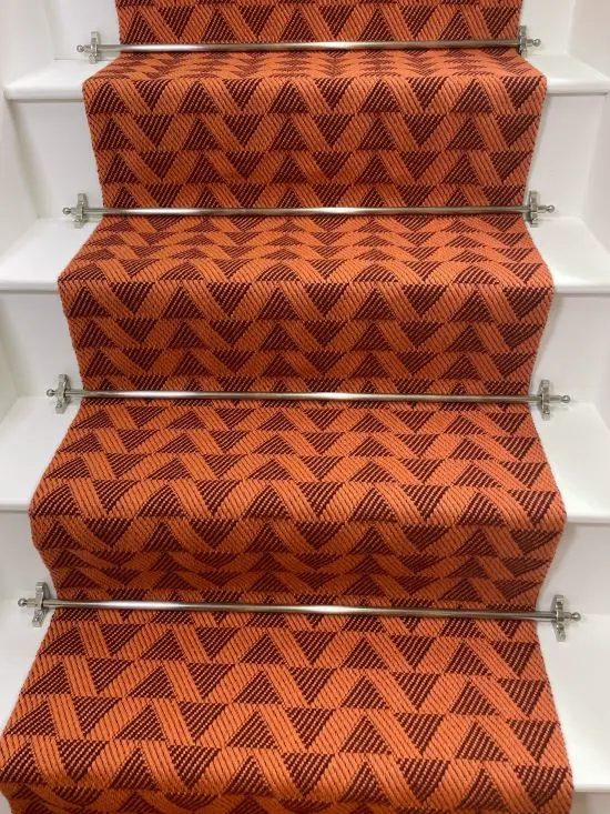 Bright orange stair runner with red triangle pattern on white wooden stairs